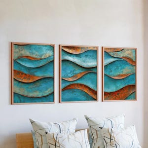 Puede incluir: Tres obras de arte abstractas enmarcadas. Cada una presenta un diseño de olas turquesas y cobrizas. Las obras de arte se exhiben en una pared blanca sobre cojines decorativos. Los marcos son de color madera clara.