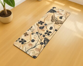 May include: A rectangular yoga mat with a floral and butterfly design. The mat features a beige background with black, brown, and gold floral and butterfly patterns. The mat is placed on a light-coloured wooden floor.