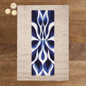 Puede incluir: Una esterilla de yoga rectangular con un diseño floral azul y blanco. La esterilla está centrada en una alfombra beige, con tres velas encendidas en la esquina superior izquierda. El diseño de la esterilla de yoga presenta un patrón simétrico de pétalos estilizados.