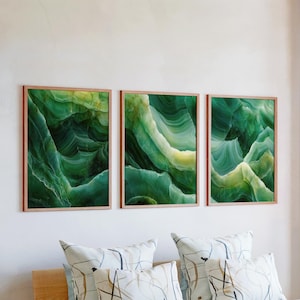 May include: Three framed wall art pieces with abstract green and yellow designs. The artwork features layered, flowing patterns reminiscent of natural stone formations. The frames are a light brown color, and the art is displayed above decorative pillows.