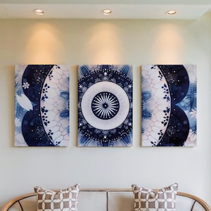 Könnte beinhalten: Drei rechteckige Wandbilder mit einem blau-weißen Mandala-Design. Die Kunstwerke sind an einer hellen Wand angebracht, über einem Sofa mit gemusterten Kissen. Die Kunstwerke zeigen ein zentrales kreisförmiges Design.