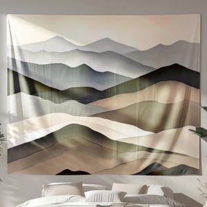 May include: A large wall tapestry featuring a watercolor painting of layered mountain ranges in shades of gray, green, and brown. The artwork has a soft, diffused light and shadow effect, creating a serene and natural aesthetic. The tapestry is hung above a bed.