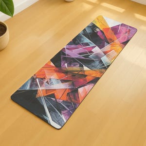 May include: A rectangular yoga mat with an abstract geometric design. The pattern features overlapping shapes in shades of orange, purple, and grey, creating a modern and artistic look. The mat is placed on a light-coloured wooden floor.