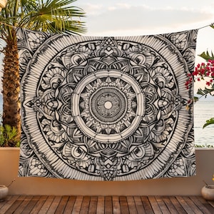 Könnte beinhalten: Schwarz-weißes Mandala-Wandteppich, der auf einem Balkon mit Blick auf das Meer hängt. Das komplizierte Design zeigt konzentrische Kreise und florale Muster. Der Wandteppich wird im Freien ausgestellt und schafft eine ruhige und künstlerische Atmosphäre.
