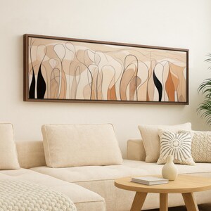 May include: Abstract art print in a rectangular brown frame. The artwork features a series of organic shapes in beige, black, and orange tones, with thin black lines outlining the forms. The art piece hangs above a beige sectional sofa.