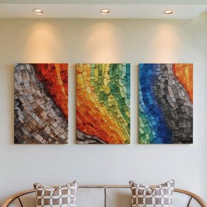 May include: Three abstract mosaic art pieces hang on a white wall. The artwork features a spectrum of colors, including red, orange, yellow, green, blue, and gray. The pieces are rectangular and mounted above a sofa with patterned pillows.