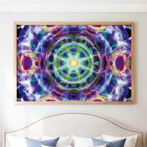 May include: A rectangular wall art print in a light wood frame featuring a vibrant, symmetrical abstract design. The artwork displays a central glowing yellow starburst surrounded by concentric rings of blue, purple, green, and white light patterns.