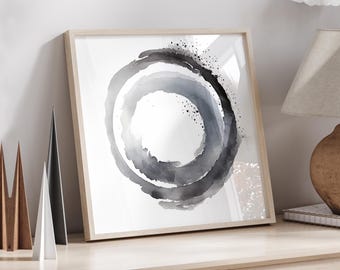 May include: Abstract art print featuring a watercolor design of overlapping gray and black circles. The artwork is framed in a light wood frame and leans against a white wall. Decorative wooden triangles are in the foreground.