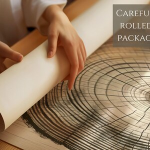 Pode incluir: Um close-up de uma m&atilde;o a enrolar uma impress&atilde;o de uma se&ccedil;&atilde;o transversal de tronco de &aacute;rvore. A impress&atilde;o est&aacute; sobre um fundo branco e tem um padr&atilde;o de gr&atilde;o de madeira natural. O texto "CAREFULLY ROLLED & PACKAGED" &eacute; vis&iacute;vel no canto superior direito da imagem.