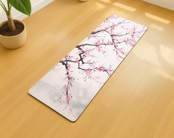 May include: A rectangular yoga mat featuring a watercolor design of a cherry blossom branch with pink flowers and black branches against a white background. The mat is on a wooden floor.