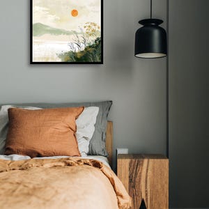 May include: A framed watercolor painting of a landscape with a large orange sun in the sky, green hills, and a body of water. The painting is hanging on a gray wall above a bed with a brown blanket and pillows.