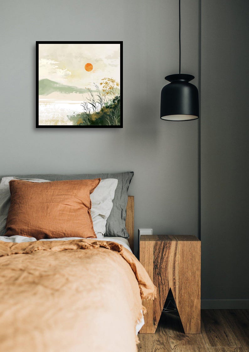 May include: A framed watercolor painting of a landscape with a large orange sun in the sky, green hills, and a body of water. The painting is hanging on a gray wall above a bed with a brown blanket and pillows.