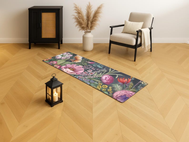 May include: A floral yoga mat with a dark background and a vibrant array of pink, purple, and yellow flowers. The mat is rectangular and lies on a wooden floor. A black lantern with a lit candle sits nearby.