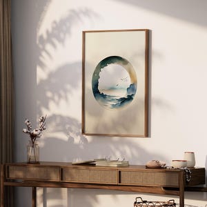 May include: A framed watercolor print featuring an abstract landscape within an oval shape. The artwork depicts a serene scene with blue and green hues, suggesting a coastal or mountain view. The frame is a warm, natural wood tone.