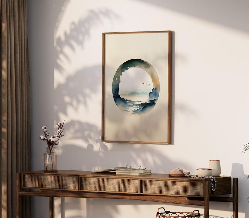 May include: A framed watercolor print featuring an abstract landscape within an oval shape. The artwork depicts a serene scene with blue and green hues, suggesting a coastal or mountain view. The frame is a warm, natural wood tone.