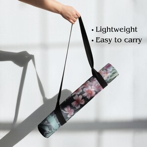 May include: A rolled-up yoga mat with a floral design, held by a black strap. The mat features pink flowers and green leaves on a dark background. The text on the image says "Lightweight" and "Easy to carry".