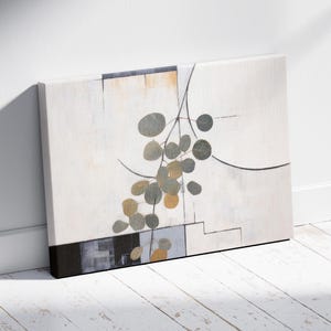 Könnte beinhalten: Abstrakte Leinwandkunst mit einem botanischen Design. Es zeigt graue und goldene kreisförmige Formen auf weißem Hintergrund, mit schwarzen Linien und geometrischen Formen. Die Leinwand wird vor einer weißen Wand und einem weißen Boden ausgestellt.