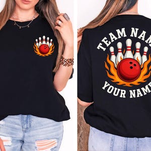 May include: A black t-shirt featuring a graphic of a red bowling ball and white pins surrounded by orange flames. The front has a small left-chest print, while the back displays the same graphic with the text "TEAM NAME" and "YOUR NAME".