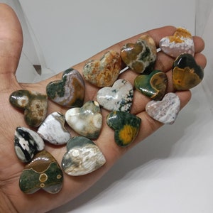 May include: A collection of 15 green, brown, and white heart-shaped polished stones. The stones have a variety of patterns and textures.
