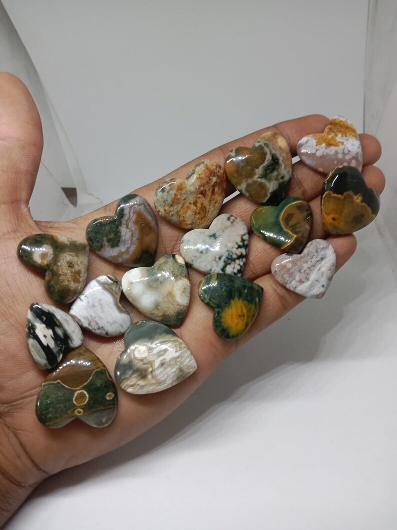 May include: A collection of 15 green, brown, and white heart-shaped polished stones. The stones have a variety of patterns and textures.