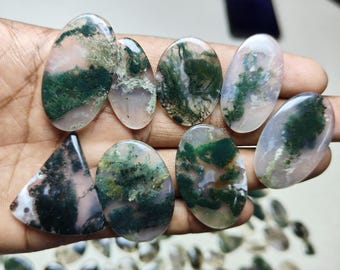 May include: A collection of moss agate cabochons in various shapes and sizes. The cabochons are a mix of green, white, and brown colours.