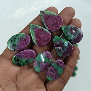 Pode incluir: Uma coleção de oito pedras preciosas em forma de lágrima, de cor verde e rosa. As pedras são lisas e polidas, com uma variedade de tons de verde e rosa.