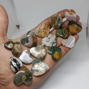 May include: A collection of 15 heart-shaped polished stones with green, brown, and white patterns. The stones are arranged in a hand.