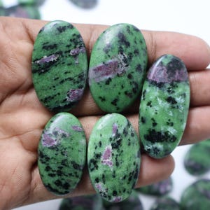 Puede incluir: Seis piedras preciosas verdes de forma ovalada con inclusiones negras y rosadas. Las piedras son lisas y pulidas.