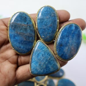 May include: A collection of blue gemstone rings with gold-colored metal settings. The rings feature oval and triangular-shaped stones. The gemstones have a textured appearance and varying shades of blue.