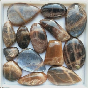 Puede incluir: Una colección de 12 cabujones de piedra solar de diferentes formas y tamaños. Las piedras son una mezcla de colores marrón, negro y dorado con un efecto brillante.