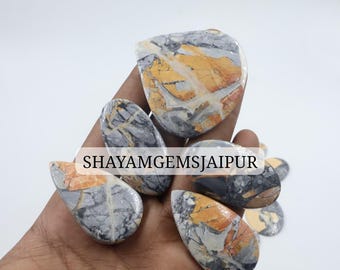 May include: A collection of polished, multi-shaped gemstones featuring a marbled pattern of grey, black, and vibrant orange-yellow veins. The stones are smooth and varied in size, with the text SHAYAMGEMSJAIPUR overlaid across the center.