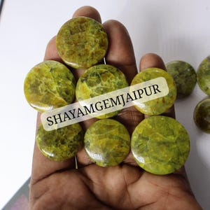 May include: A collection of round, polished, chartreuse-colored gemstones with intricate, web-like veining patterns throughout each stone. The stones feature a smooth, glossy finish and are displayed together. The text SHAYAMGEMJAIPUR is visible.