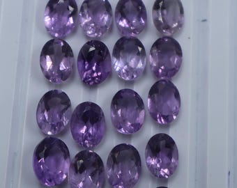 Könnte beinhalten: Zwanzig ovale Amethyst-Edelsteine in verschiedenen Violetttönen. Die Edelsteine sind in vier Reihen zu fünf angeordnet.