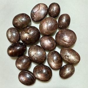 May include: A collection of 16 brown and pink star ruby cabochons. The stones are smooth and polished, with a variety of shapes and sizes.