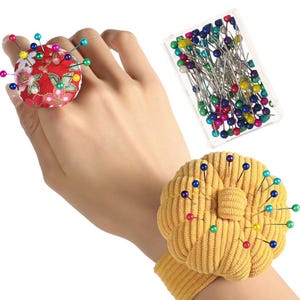 Pu&ograve; includere: Un cuscinetto per spilli floreale rosso indossato al dito, un cuscinetto per spilli giallo da polso e un contenitore di plastica trasparente con spilli colorati. I cuscinetti per spilli sono riempiti con spilli di vari colori.