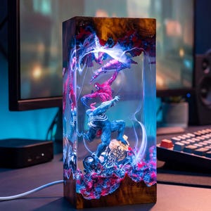May include: A rectangular lamp made of dark wood and clear resin, featuring an internal diorama of the characters Venom and Carnage in a dynamic pose. The piece is illuminated from within by blue and white light, with red and blue textured accents.