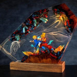May include: A unique resin lamp featuring two action figures in a dynamic pose, set against a backdrop of colorful, textured materials. The lamp has a wooden base and a clear resin body with embedded details and a warm glow.