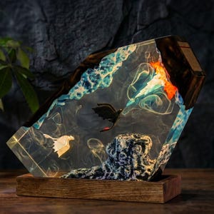 May include: A rectangular resin lamp featuring a dark wood frame and base. Inside the clear resin, a black dragon and a white dragon fly above a textured rock formation. Swirls of blue and orange resin mimic water and fire effects throughout.