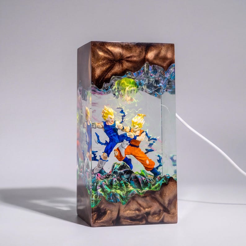 Op de afbeelding: Een rechthoekige harslamp met twee anime-figuren in een dynamische gevechtshouding. De figuren zijn ingesloten in heldere hars met een bronskleurige, getextureerde boven- en onderkant en blauwe energie-effecten.