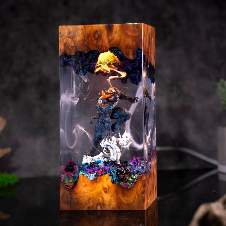 May include: A rectangular wooden block with a detailed sculpture encased in clear resin. The sculpture depicts a figure in a dynamic pose, with vibrant colors and intricate details. The wood has a natural grain, and the resin features colorful accents.
