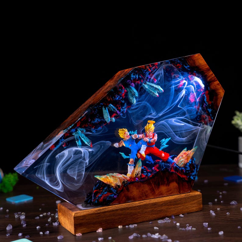 Pu&ograve; includere: Una lampada decorativa con base in legno e un blocco di resina contenente due personaggi anime in una posa di combattimento dinamica. La resina presenta effetti di fumo bianco vorticoso, accenti blu e rossi e forme cristalline illuminate.
