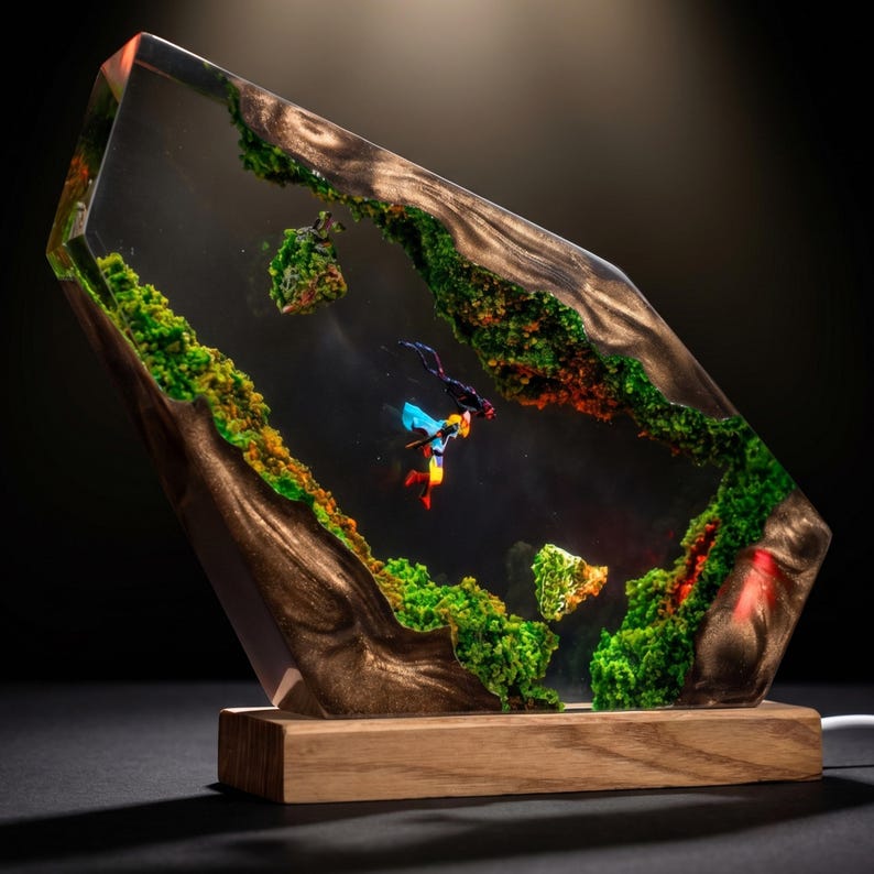 May include: A rectangular resin lamp featuring a dark wood frame with embedded green moss and a miniature scuba diver figurine suspended in the clear center. The piece is mounted on a solid light-colored wooden base with an integrated light source.