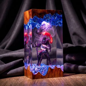 May include: A rectangular resin and wood lamp featuring a clear central chamber. Inside, a miniature figure stands before a dark armored entity with a red plume. The top and bottom edges are crafted from natural wood with jagged blue resin accents.