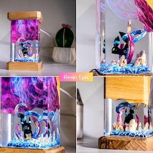 May include: A rectangular resin lamp featuring a black Umbreon figure encased in clear resin with swirling purple and pink smoke effects. The lamp has a wooden base and top, with a base of blue and white textured material resembling water.