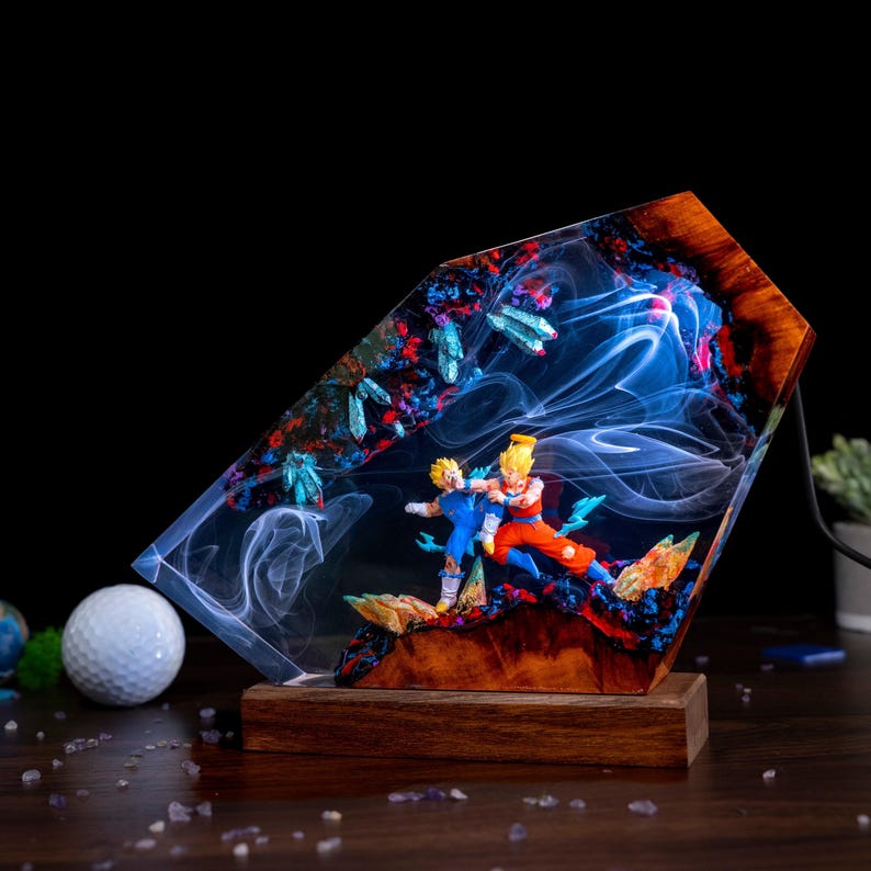 Pu&ograve; includere: Una lampada decorativa con base in legno e un diorama in resina che raffigura due personaggi anime in posa da combattimento. La resina contiene effetti di fumo bianco vorticoso, accenti blu cristallini ed elementi scuri in una cornice di legno.