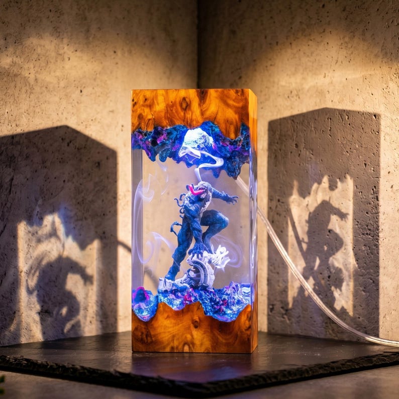 May include: A rectangular wooden lamp with a resin core featuring a blue and black action figure. The wood has a natural grain pattern with shades of brown and orange. The resin has blue and purple accents, and the lamp is lit from within.