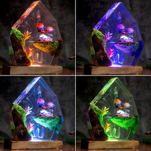 May include: A pentagonal resin lamp featuring a miniature landscape with a floating mossy island, a small panda figure, and colorful artificial plants. The clear resin structure is mounted on a rectangular wooden base and illuminated by LED lights.