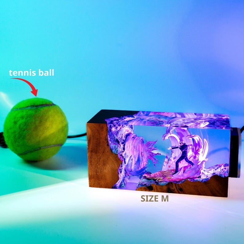 May include: A tennis ball next to a wooden block with a colorful, illuminated scene inside. The scene depicts a figure in a dark suit. The block is labeled "SIZE M".