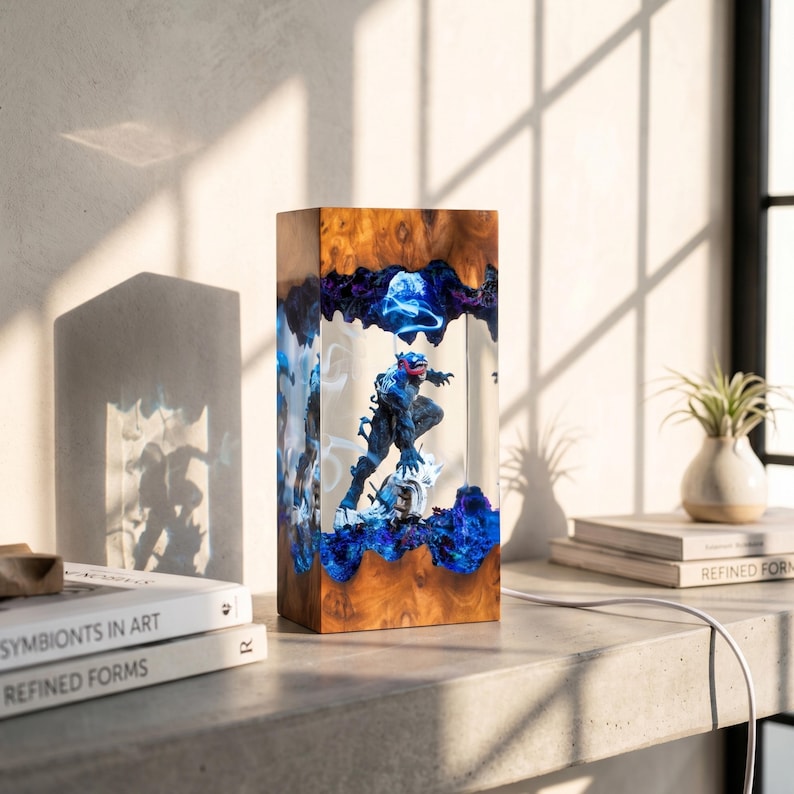May include: A rectangular wooden lamp with a superhero figure encased in clear resin. The lamp features a wood grain exterior, blue and purple resin accents, and a white power cord. The superhero figure is dark blue with red accents.