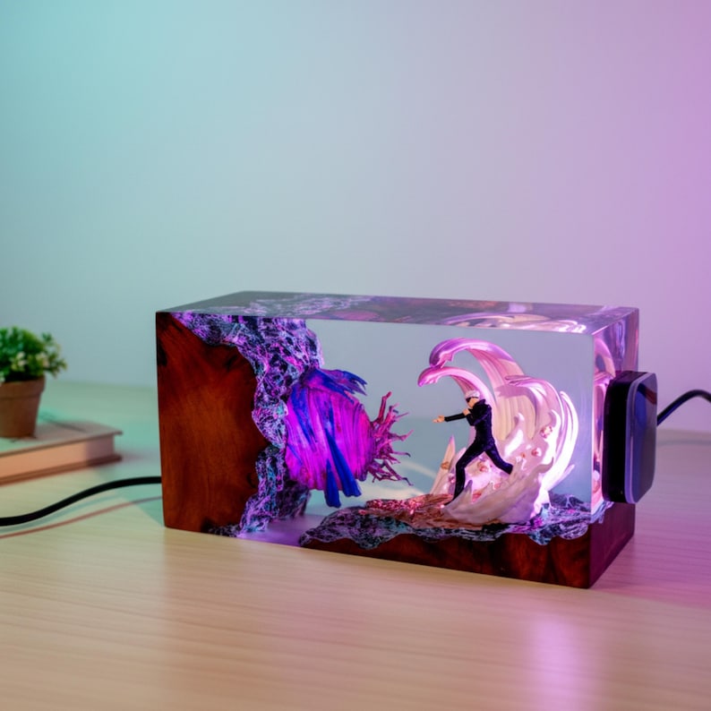 May include: A rectangular resin and wood lamp featuring a miniature figure in a dynamic pose surrounded by swirling white energy effects. A glowing purple orb is embedded within the resin, illuminated by internal lights, with a black power cord.